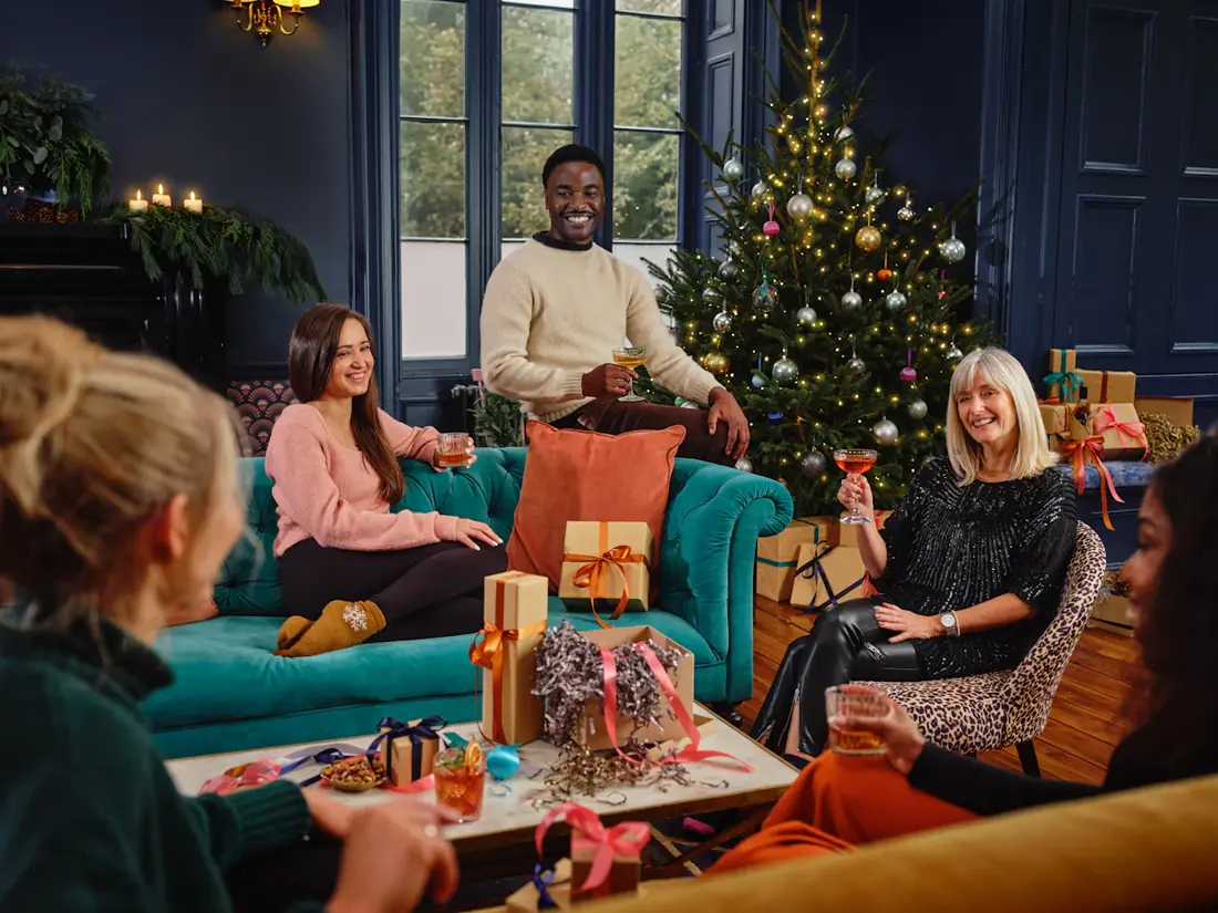 Friends on sofas beside a decorated tree at a holiday party